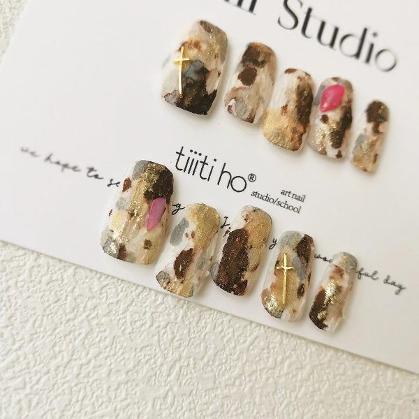 Artistic press-on nails with a gold and brown marble design, displayed on a white card from Tiiti Ho Nail Studio.