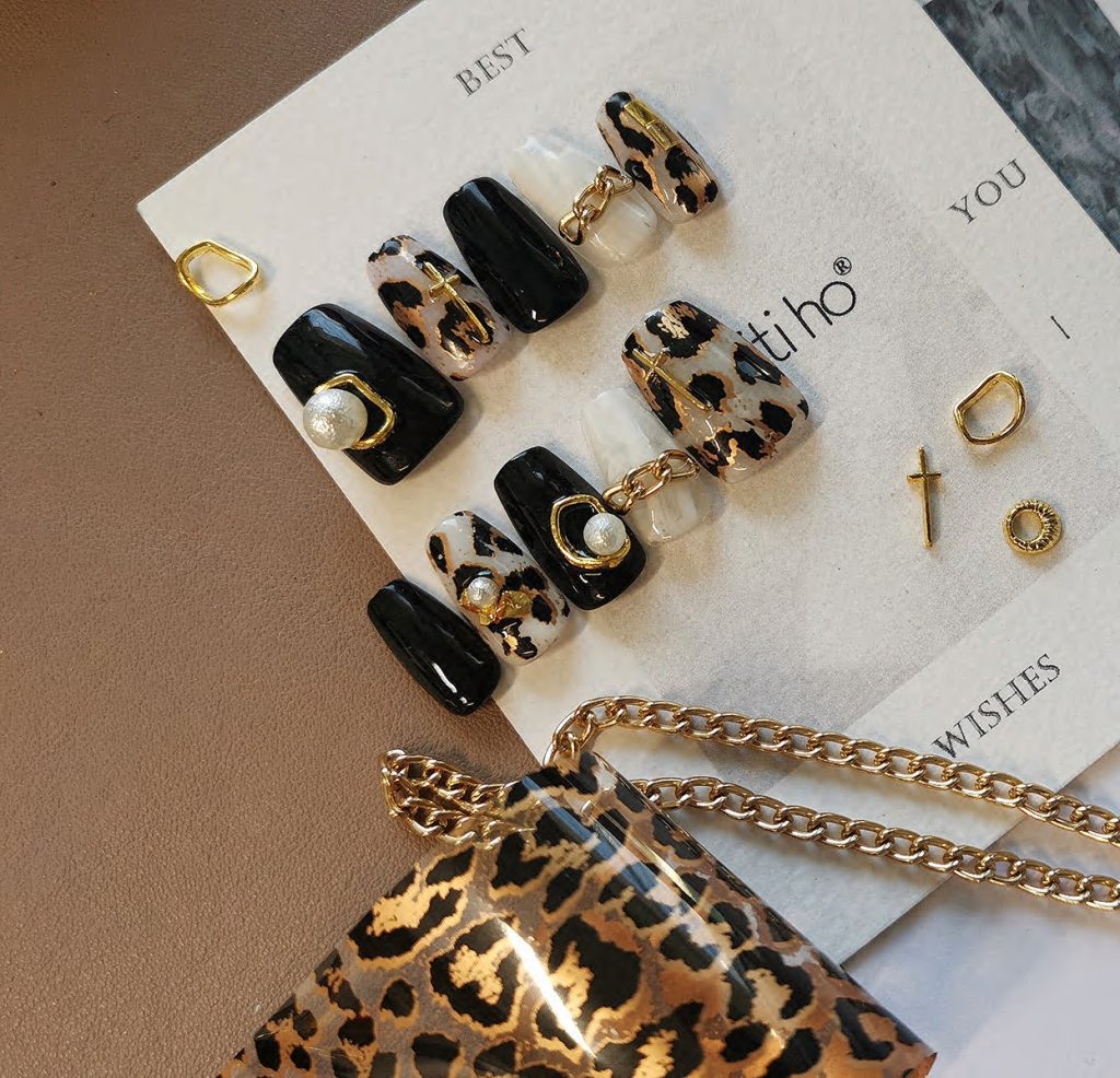 Chic press-on nails with black and leopard print design, featuring gold and pearl accents, displayed on a card from EasyPressOn.com : Tiiti Ho Nail Studio.