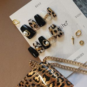 Chic press-on nails with black and leopard print design, featuring gold and pearl accents, displayed on a card from EasyPressOn.com : Tiiti Ho Nail Studio.